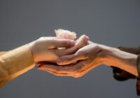 close up of man and woman touching hands and woman holding a rose flower head